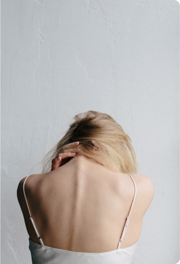 View of a woman's back where her hands are clasped behind her neck leaning forward.