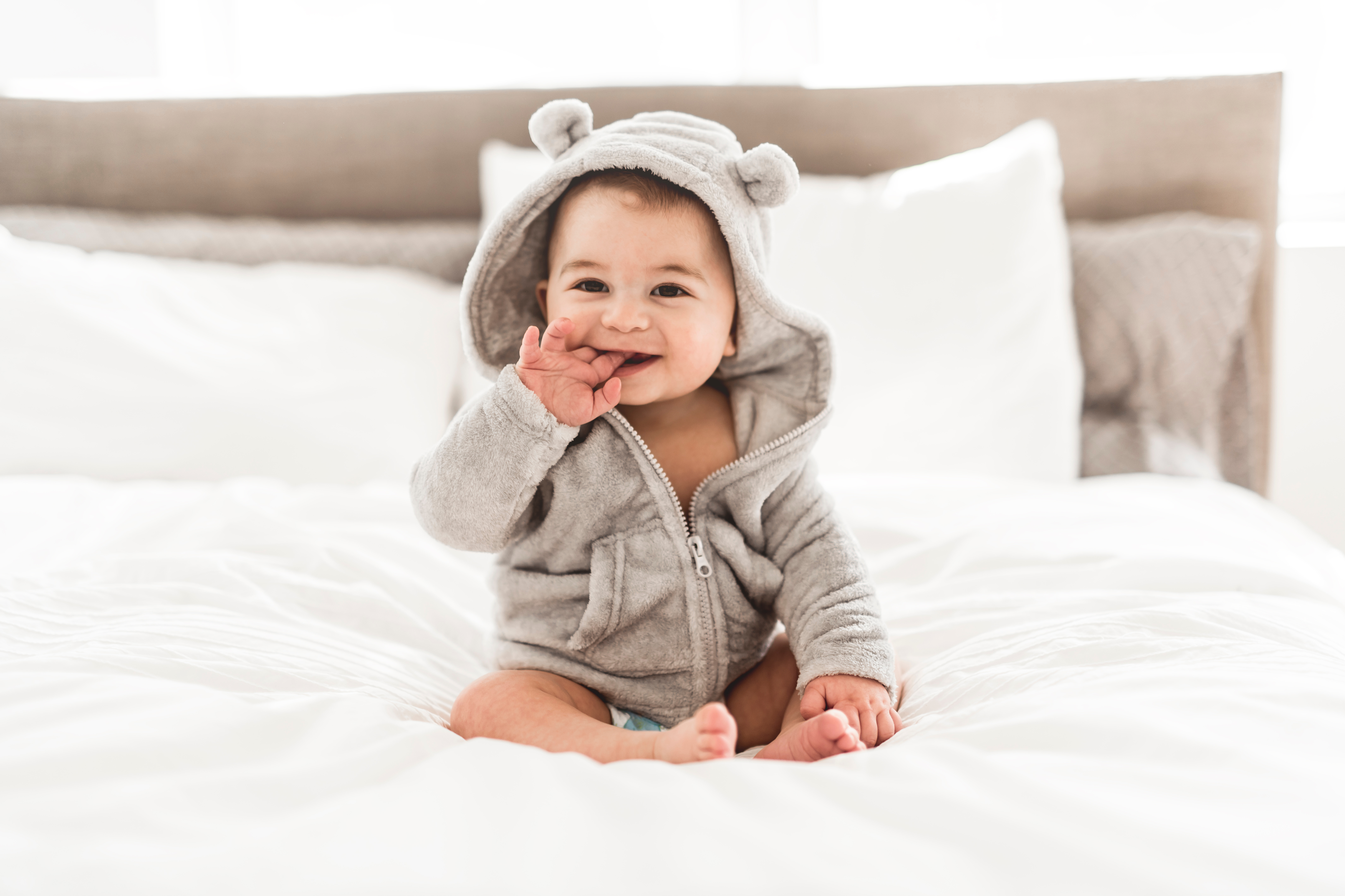Baby sitting on the bed with a hooded bath towel with its fingers in its mouth