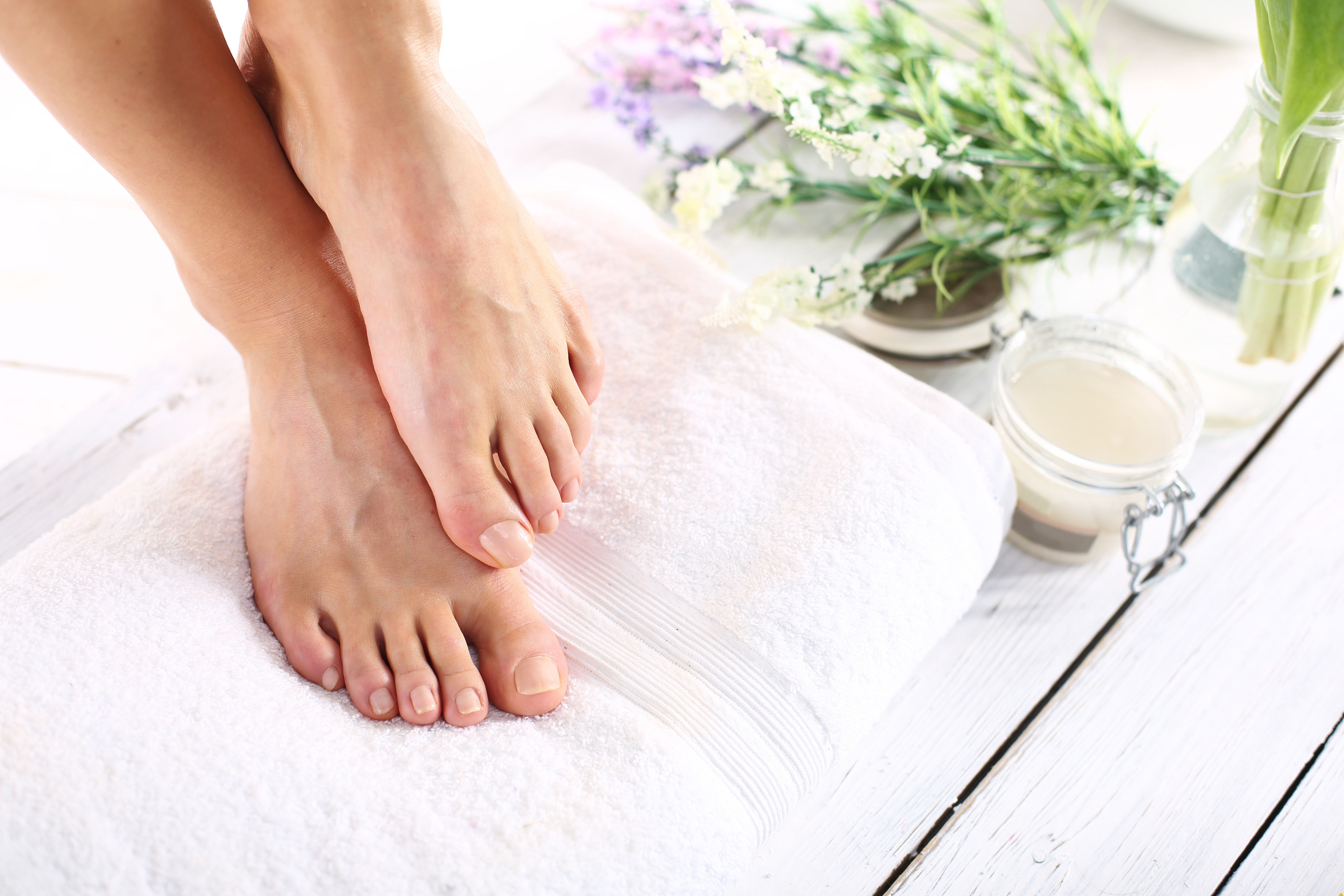 Image of a woman's feet as she is stepping on a towel with spa items beside her.