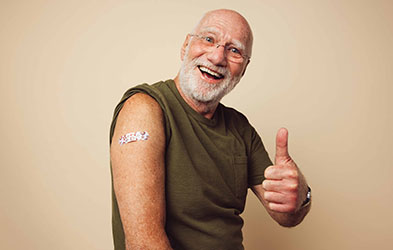 Happy old man showing vaccinated spot with band-aid on his right arm and left hand thumb