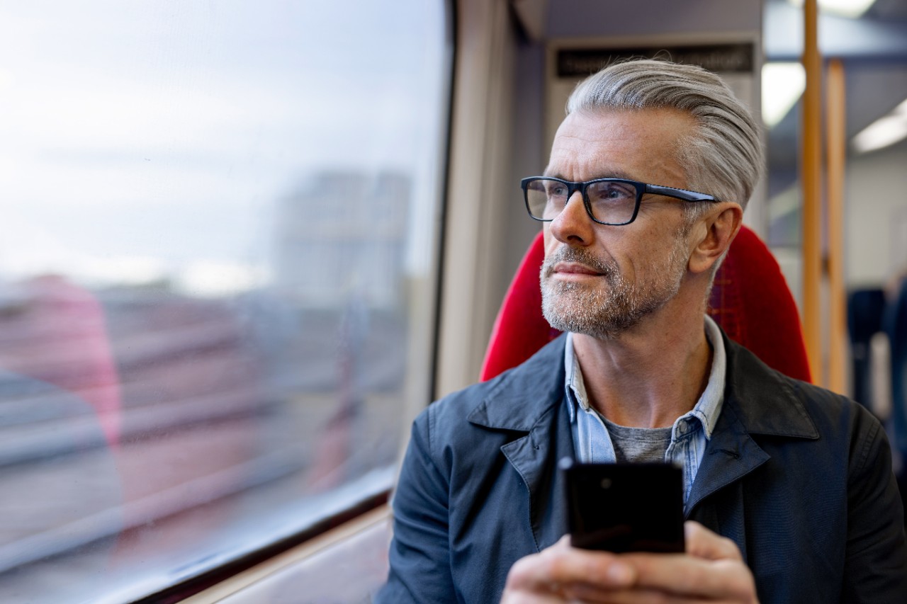 Thoughtful man using his phone while riding on a train and looking through the window